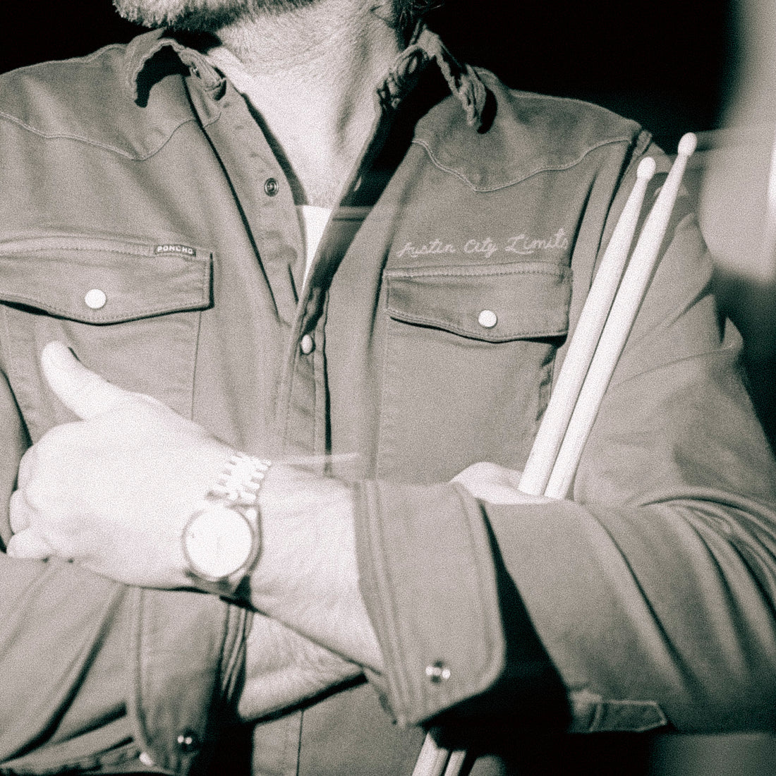 Person wearing a shirt with 'Austin City Limits' branding, holding drumsticks.