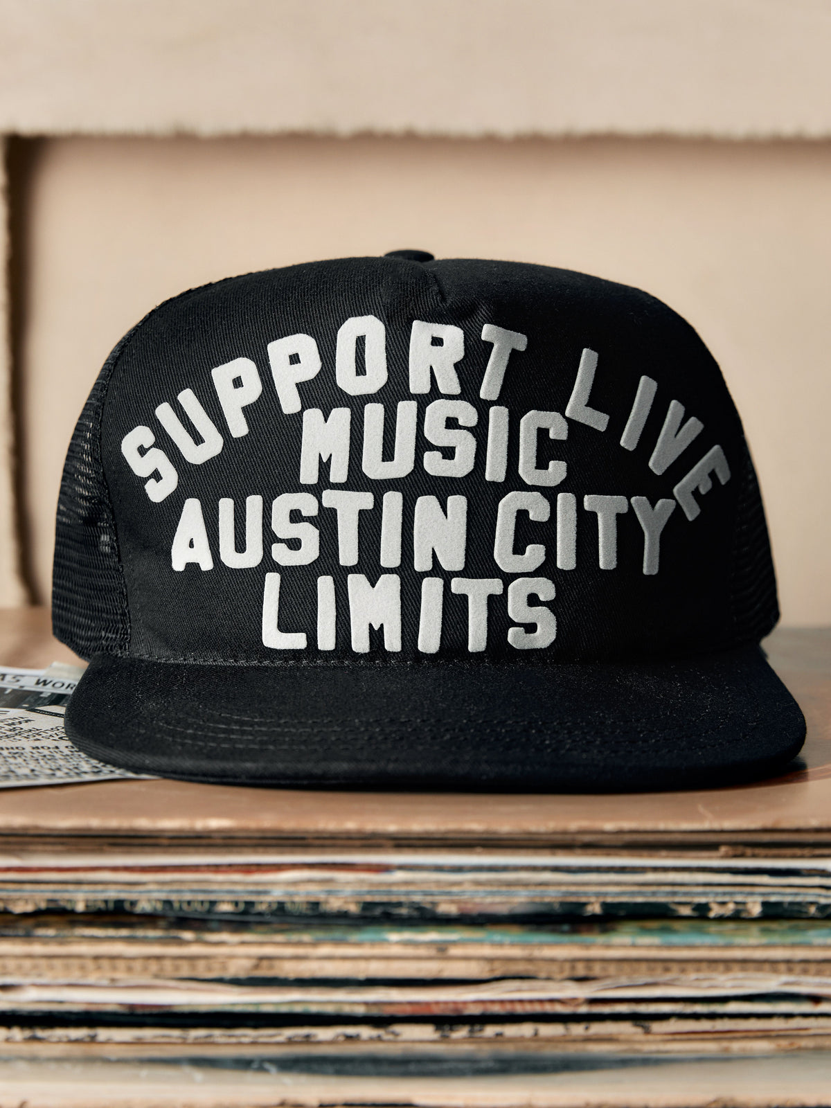 Black cap with 'Support Live Music Austin City Limits' text on a stack of records.