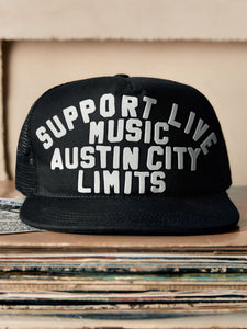 Black cap with 'Support Live Music Austin City Limits' text on a stack of records.