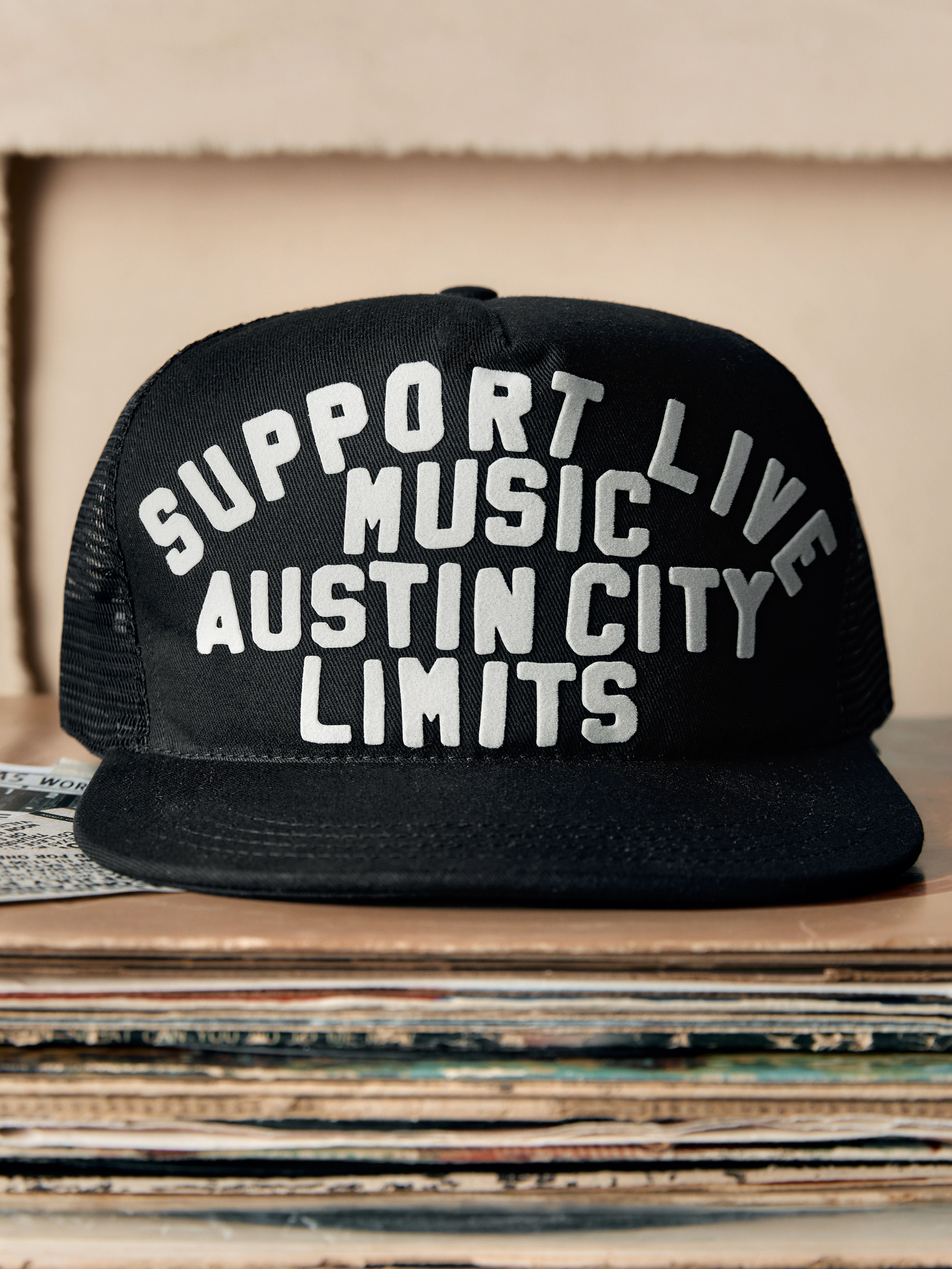 Black cap with 'Support Live Music Austin City Limits' text on a stack of records.