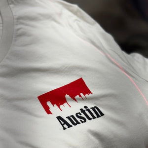 White shirt with a red and black 'Austin' logo of the Austin City Limits skyline with a cowboy font of Austin