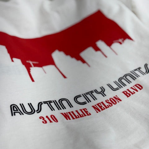 White t-shirt with red and black graphic design of Austin City Limits and Austin TX skyline on a white background with our address 310 Willie Nelson Blvd. 